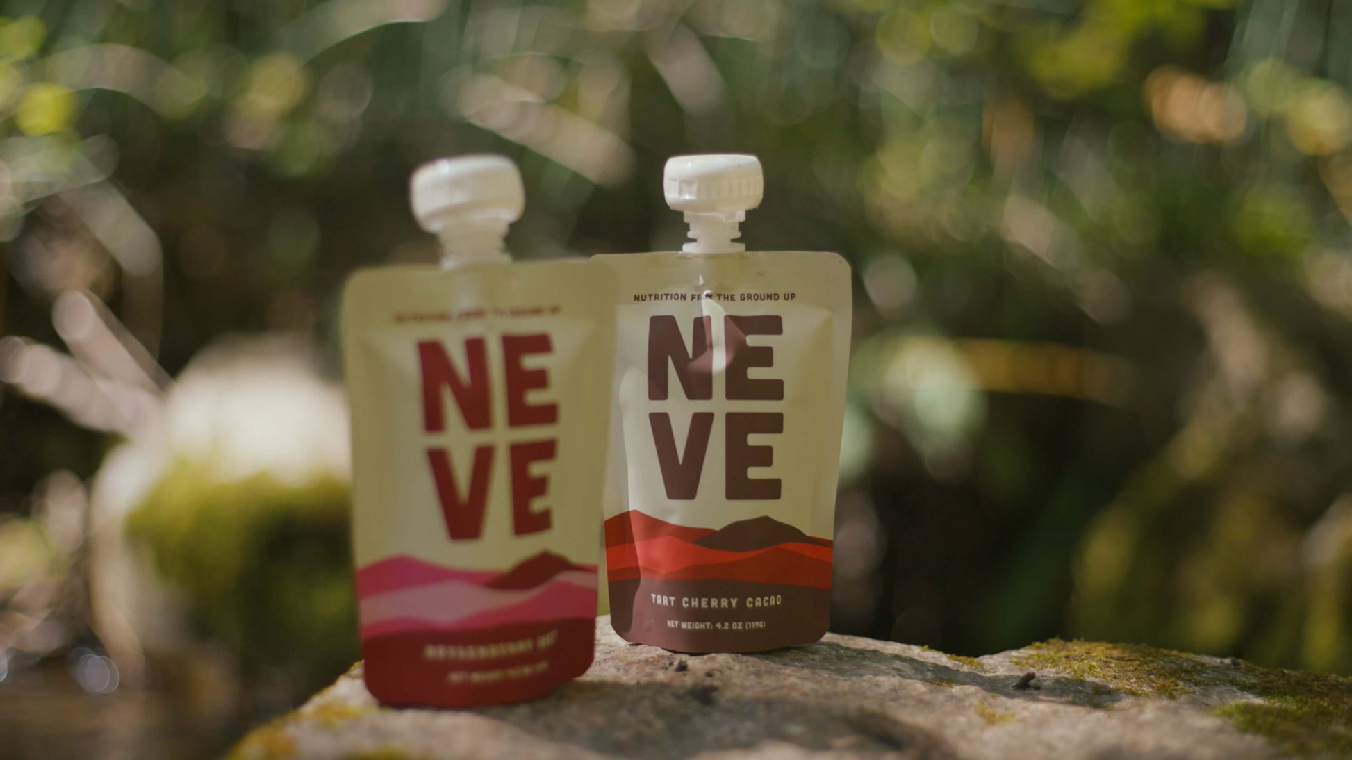 Two Neve Smoothie Pouches, Boysenberry Beet and Tart Cherry Cacao, sitting on a rock.