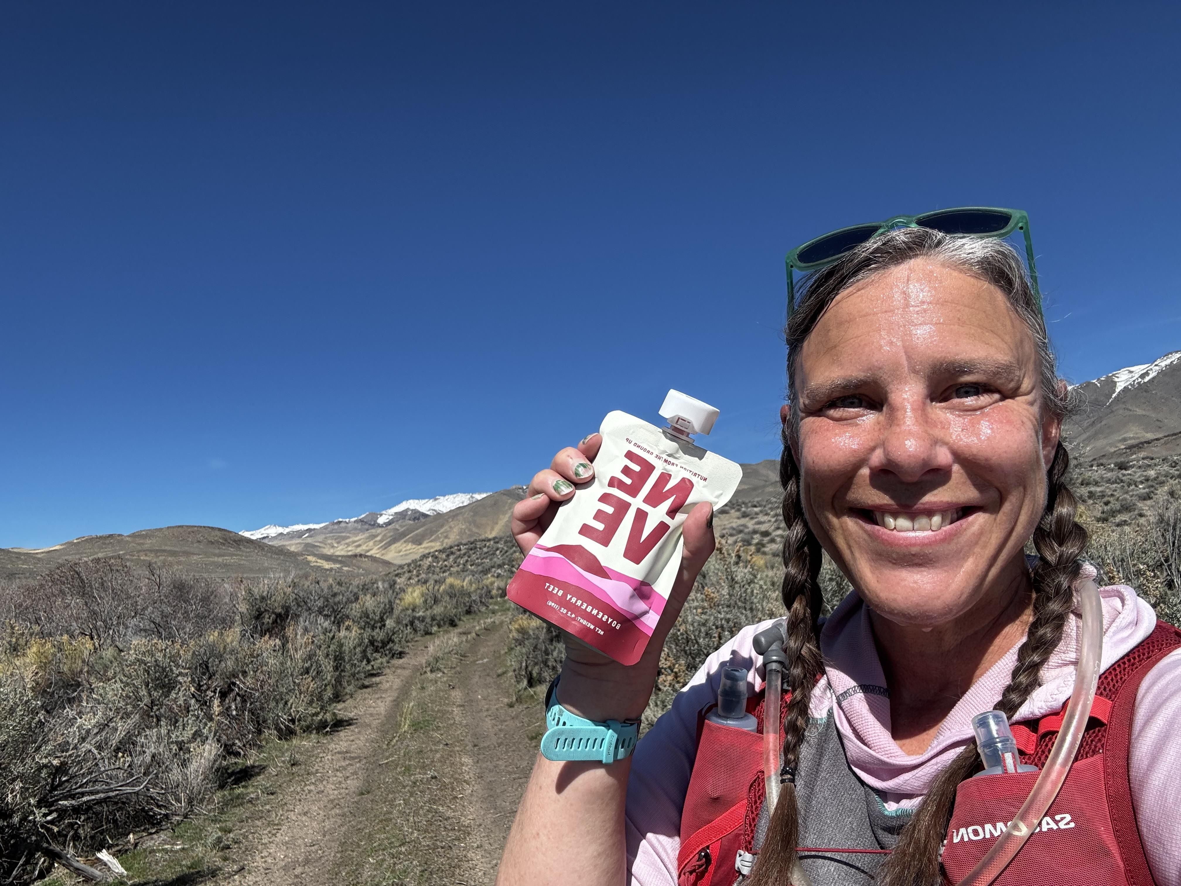 Trail runner holds up Neve Boysenberry Beet Smoothie pouch on a trail run as a source of carbs for runners