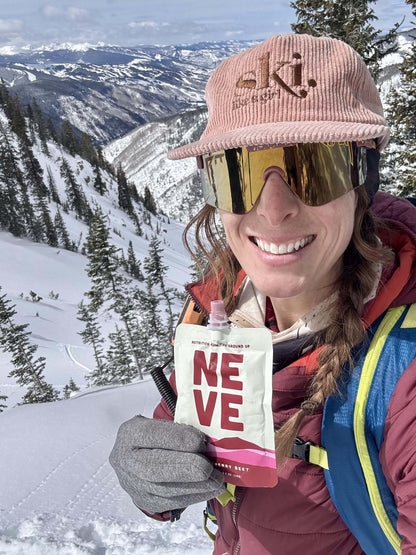 Backcountry skier holds up Neve Boysenberry Beet smoothie pouch in the backcountry
