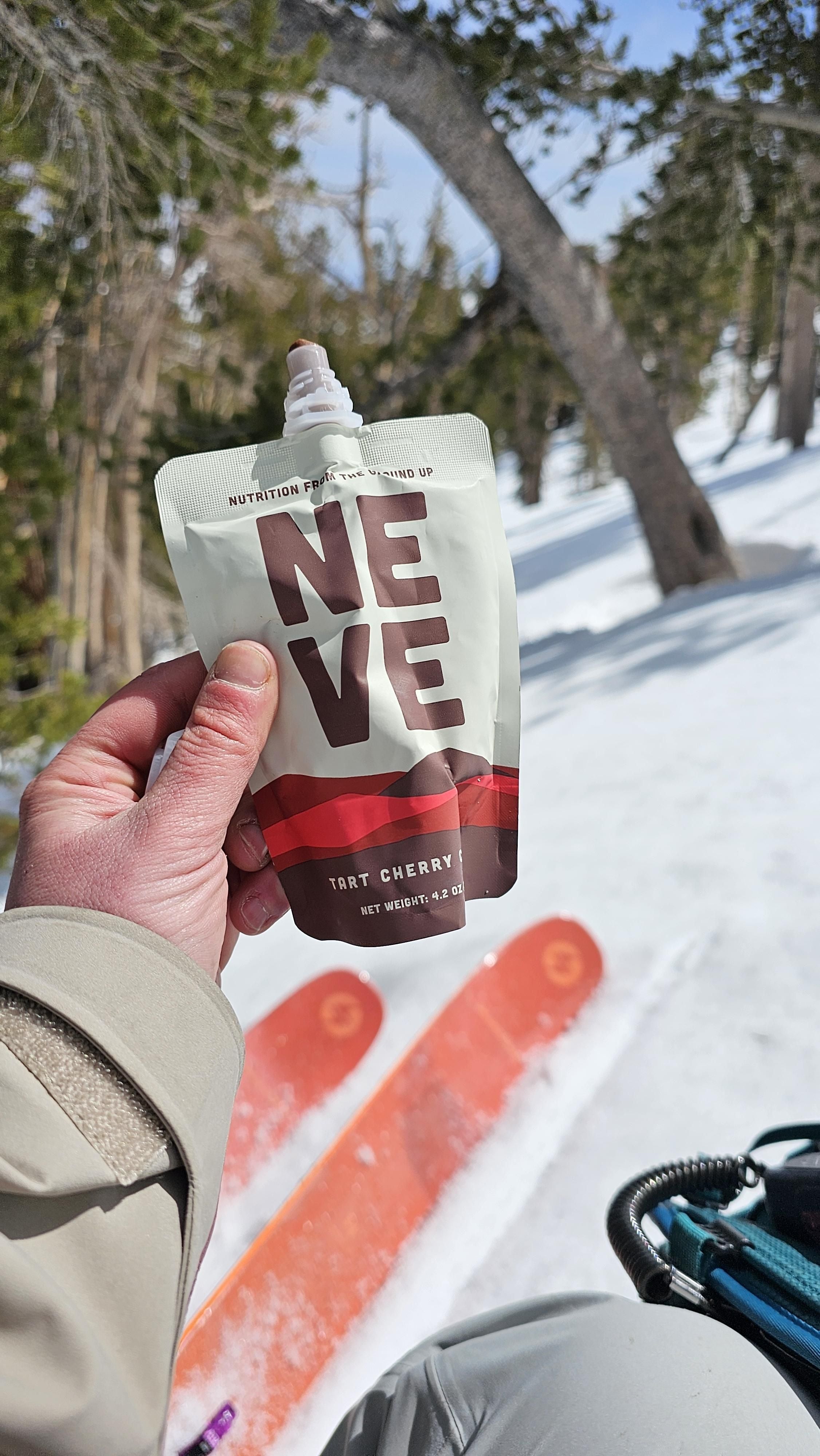 Skier holding up Tart Cherry Cacao Neve pouch in the backcountry