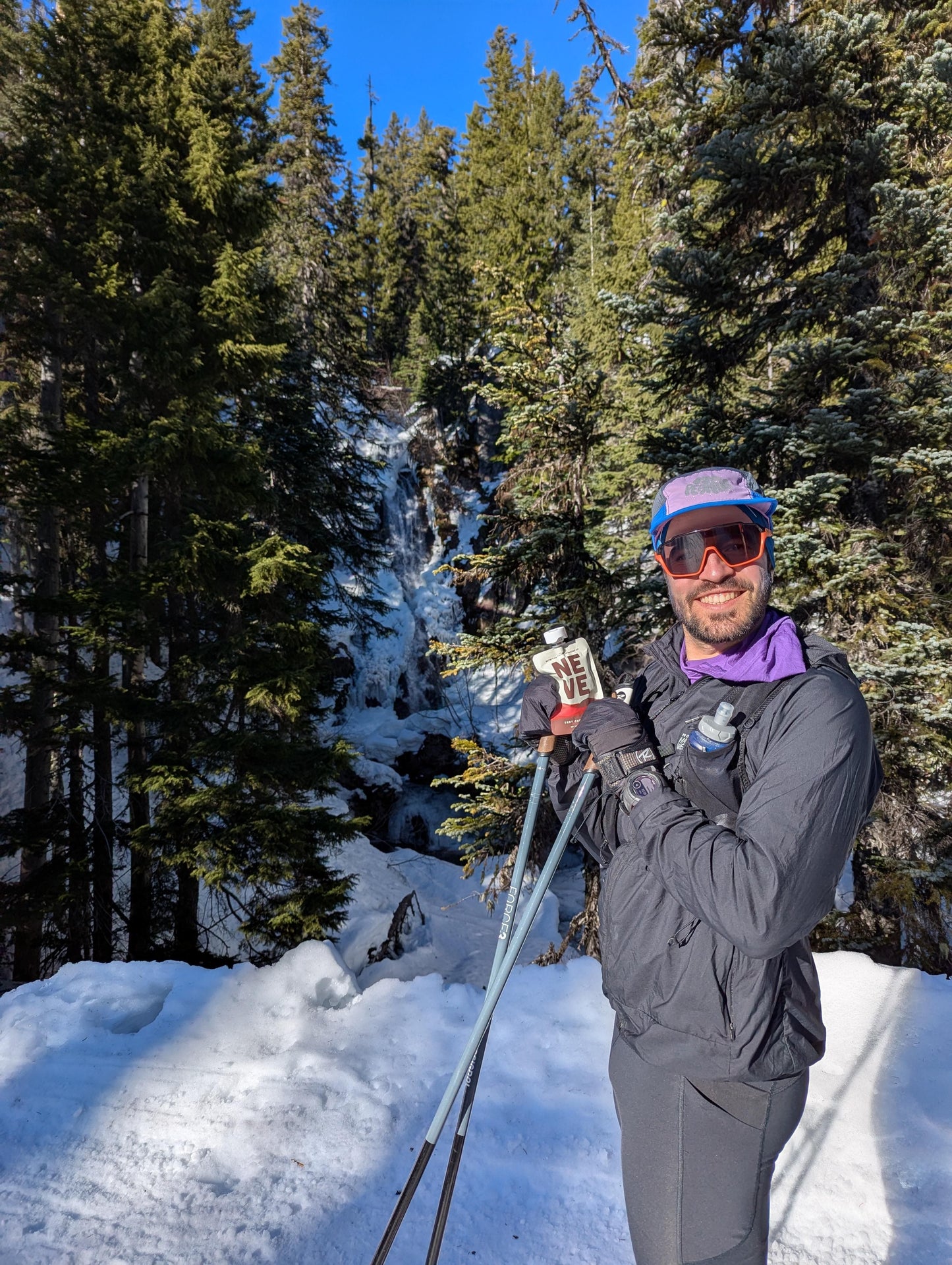 Cross country skier holds up Neve's Tart Cherry Cacao recovery smoothie pouch as cross country skiing fuel.